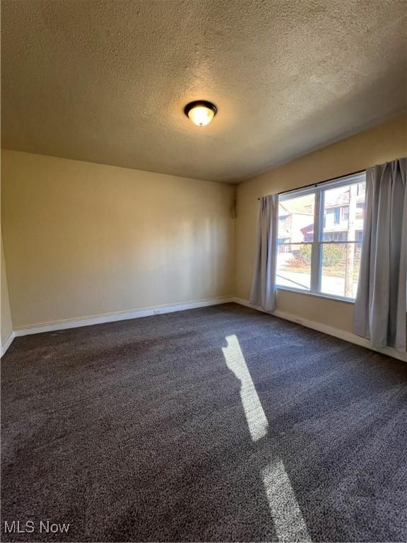 spare room with baseboards, dark carpet, and a textured ceiling