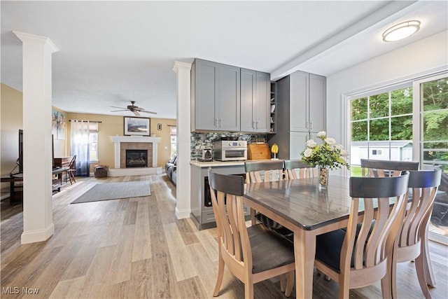 dining space with light wood-style flooring, a ceiling fan, a fireplace, a toaster, and decorative columns