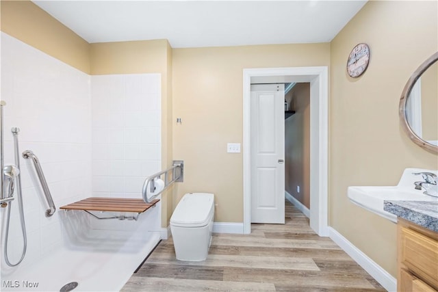 bathroom featuring wood finished floors, baseboards, tiled shower, a sink, and toilet