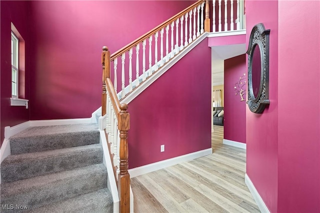 staircase featuring a high ceiling, baseboards, and wood finished floors