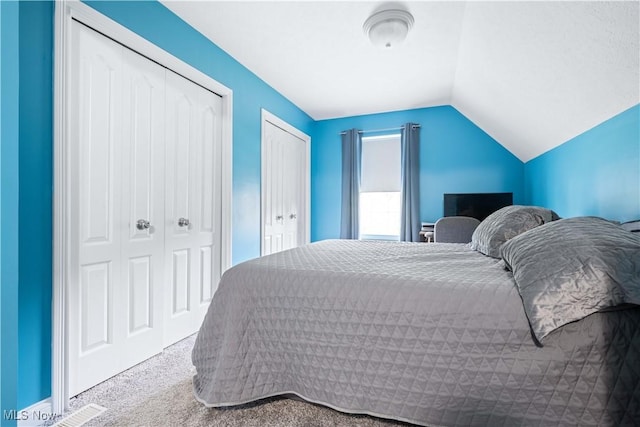 carpeted bedroom with visible vents, two closets, and vaulted ceiling