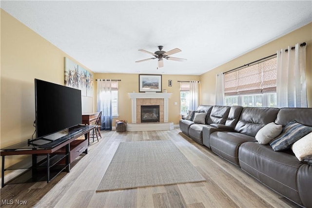 living room with light wood-style flooring, a tile fireplace, baseboards, and a ceiling fan