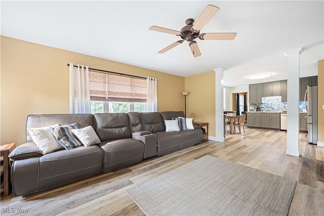 living room with decorative columns, baseboards, a ceiling fan, and light wood finished floors