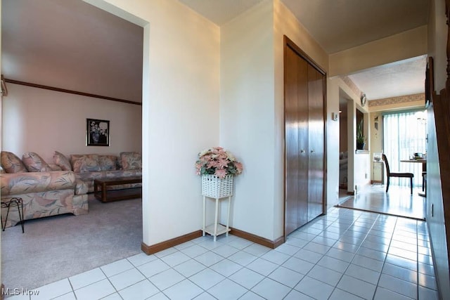 hallway featuring baseboards, light carpet, and light tile patterned flooring