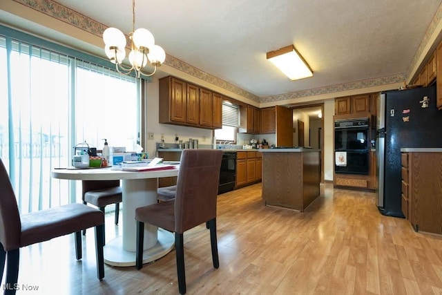 kitchen with brown cabinets, black appliances, light wood-style flooring, a center island, and a chandelier