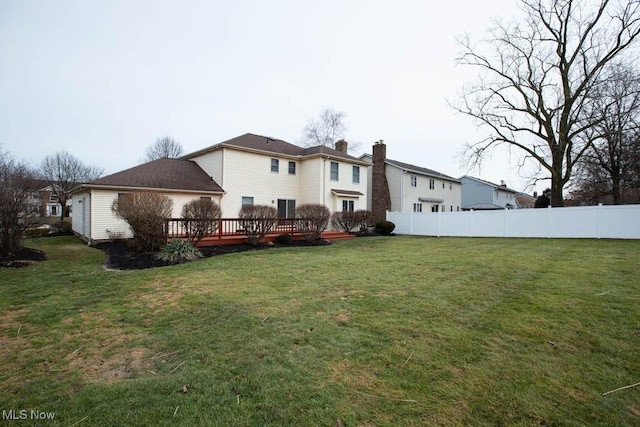 rear view of property featuring a deck, a yard, fence, and a chimney