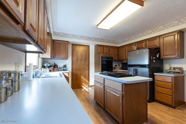 kitchen featuring black appliances, a sink, a kitchen island, light wood-style floors, and light countertops