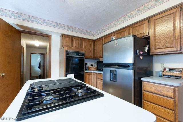 kitchen featuring a textured ceiling, black appliances, brown cabinetry, and light countertops