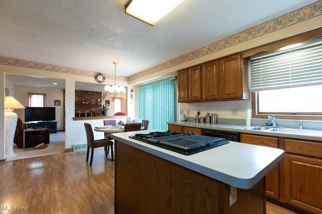 kitchen with brown cabinetry, an inviting chandelier, a sink, black appliances, and a center island