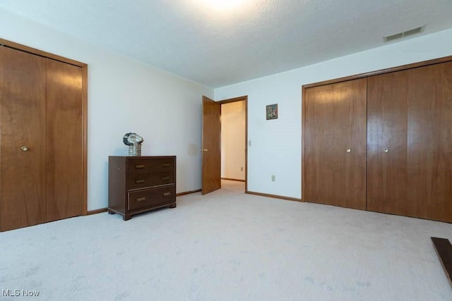 unfurnished bedroom featuring visible vents, light colored carpet, a textured ceiling, and baseboards