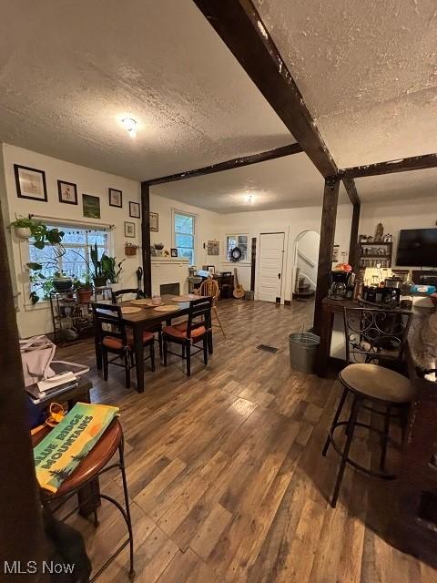 dining space with beamed ceiling, wood finished floors, and a textured ceiling