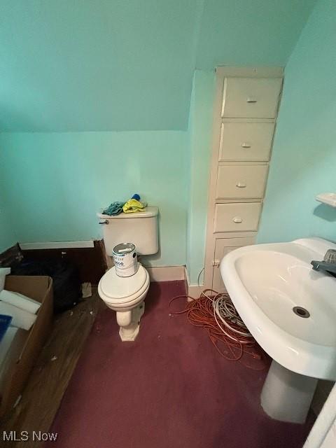 bathroom featuring baseboards, toilet, lofted ceiling, and a sink