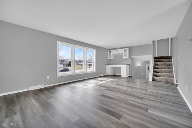 unfurnished living room featuring stairs, dark wood-type flooring, visible vents, and built in study area