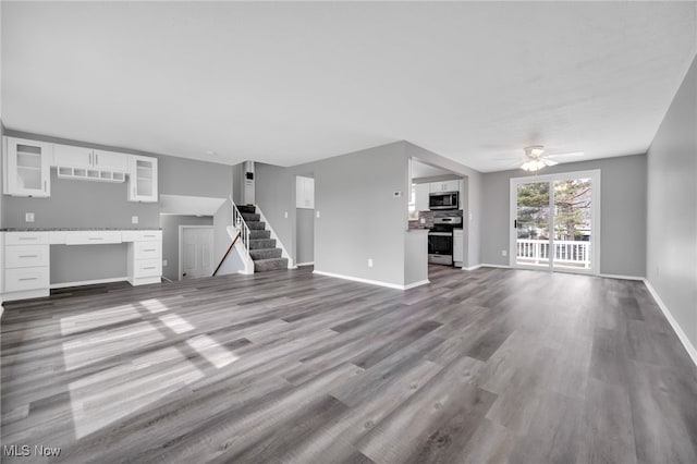 unfurnished living room featuring stairway, wood finished floors, baseboards, and ceiling fan