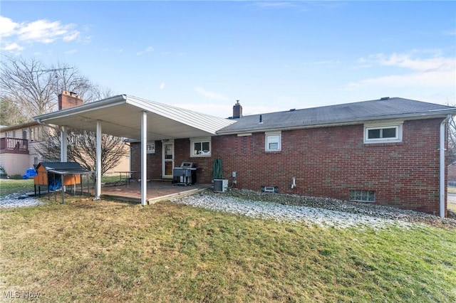 rear view of house featuring a yard, a patio, brick siding, and a chimney