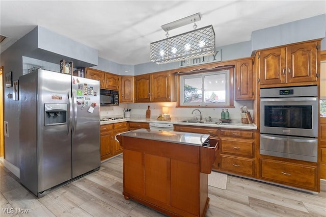 kitchen with a warming drawer, a sink, stainless steel appliances, brown cabinetry, and light wood finished floors