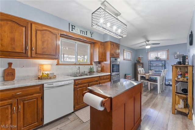 kitchen with a sink, white dishwasher, light wood finished floors, and brown cabinets