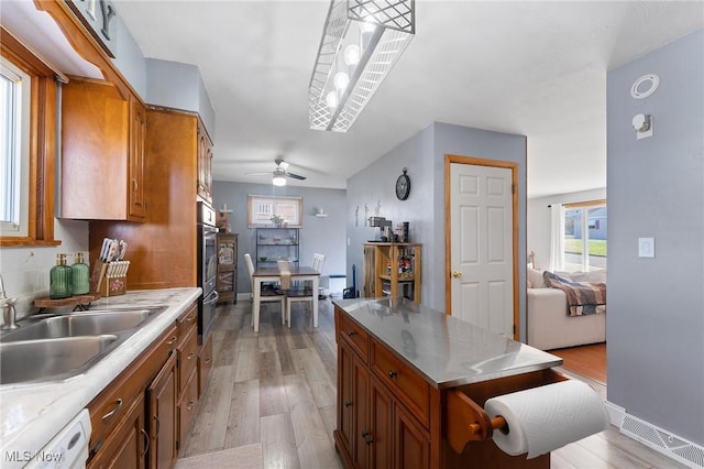 kitchen with dishwasher, light wood-style flooring, brown cabinetry, and a sink