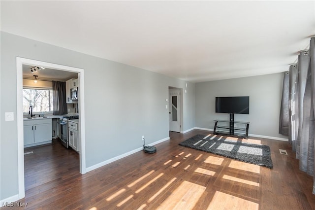 unfurnished living room with dark wood-style floors, visible vents, baseboards, and a sink