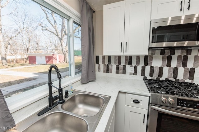 kitchen featuring a sink, stainless steel appliances, decorative backsplash, and white cabinetry