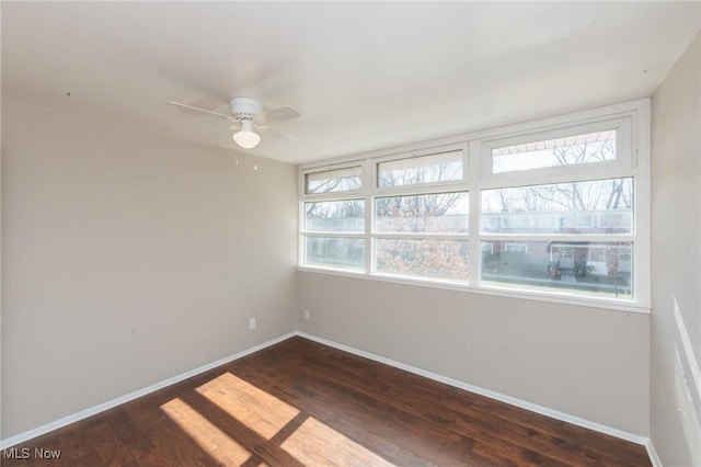 spare room featuring baseboards, ceiling fan, and dark wood-style flooring