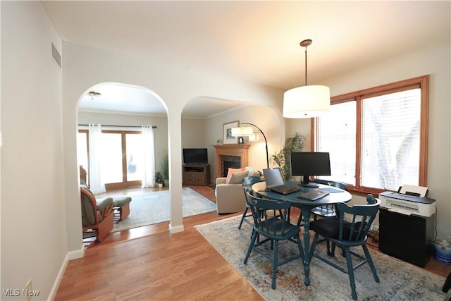 dining room featuring visible vents, arched walkways, light wood-style floors, a fireplace, and baseboards