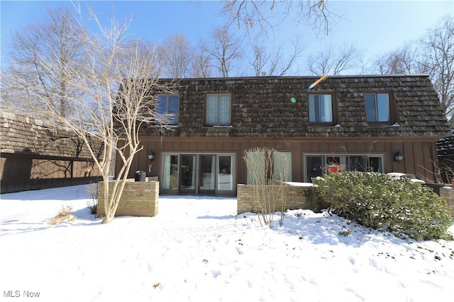 snow covered rear of property featuring mansard roof and board and batten siding