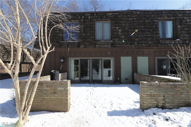 snow covered back of property with mansard roof and board and batten siding