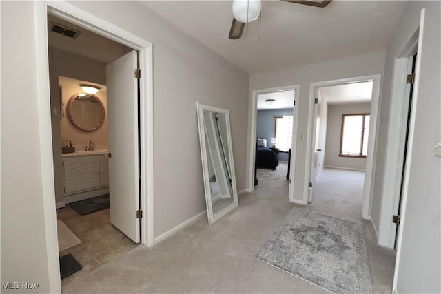 hallway with carpet flooring, baseboards, visible vents, and a sink