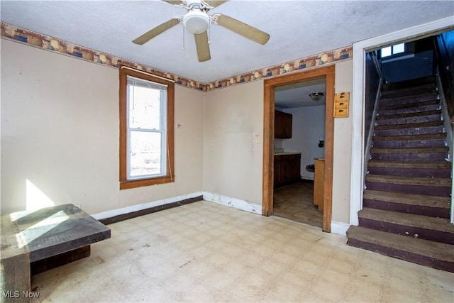 spare room featuring a ceiling fan, baseboards, stairs, a textured ceiling, and tile patterned floors