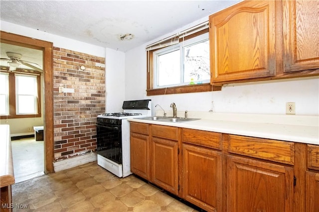 kitchen featuring brick wall, gas range, light countertops, a ceiling fan, and a sink