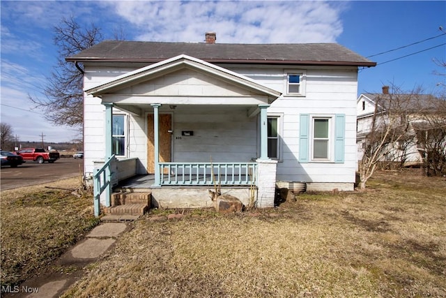 view of front of house with a front yard, covered porch, and a chimney