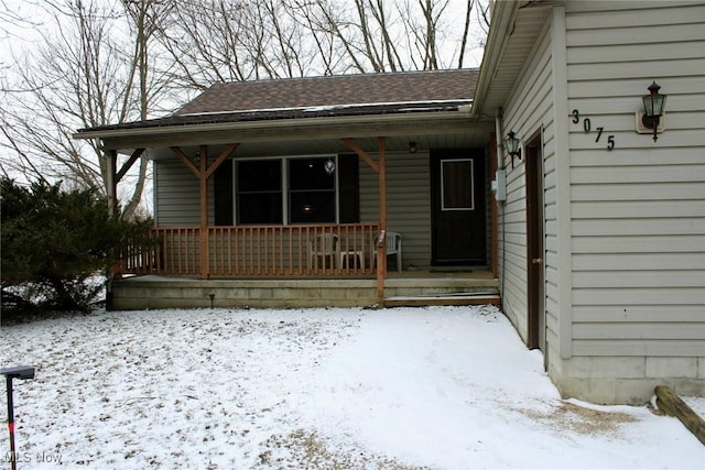 snow covered property entrance featuring roof with shingles and covered porch