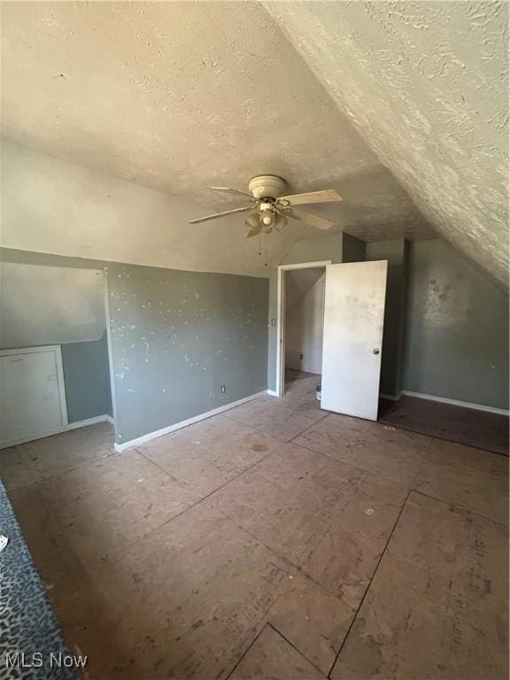 additional living space with a textured ceiling, a ceiling fan, baseboards, and vaulted ceiling