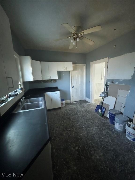kitchen featuring a sink, dark countertops, ceiling fan, and white cabinetry
