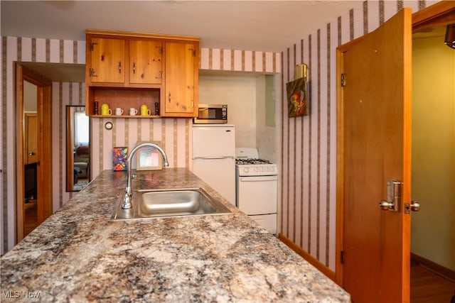 kitchen with a sink, wallpapered walls, brown cabinets, white appliances, and open shelves