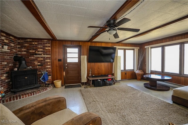 living room with wooden walls, a wood stove, ceiling fan, and a baseboard radiator