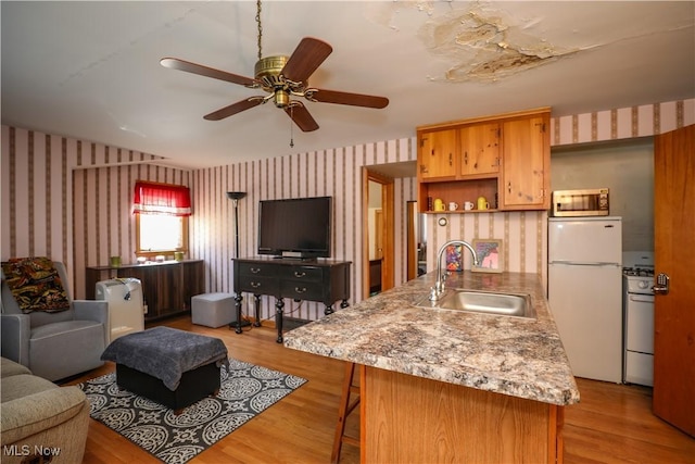 kitchen with light wood finished floors, white appliances, wallpapered walls, and a sink