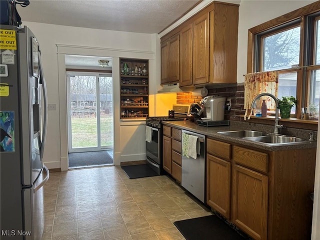 kitchen featuring dark countertops, under cabinet range hood, brown cabinets, stainless steel appliances, and a sink