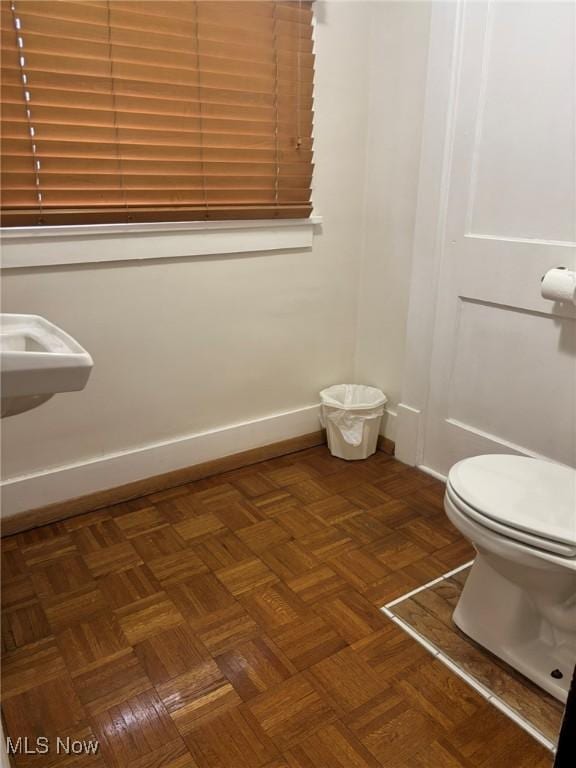 half bath featuring toilet, baseboards, and a sink