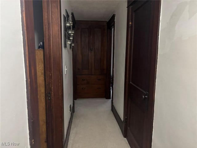 hall featuring baseboards and light colored carpet