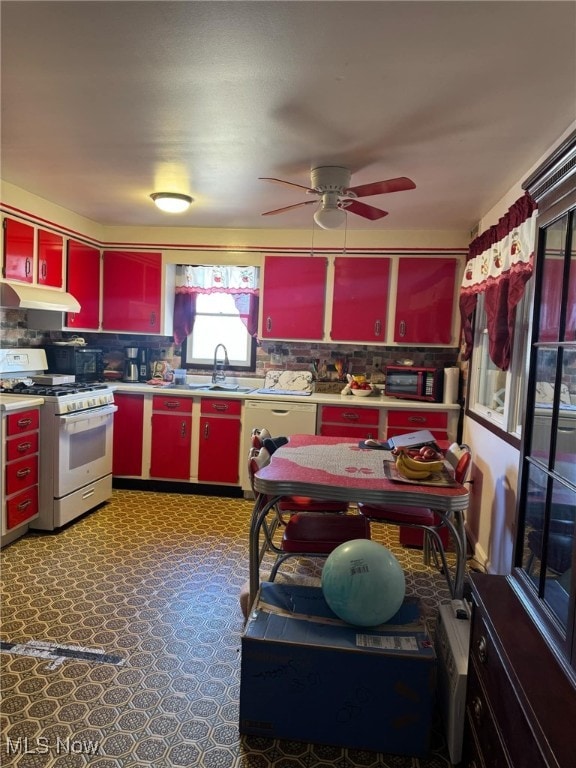 kitchen featuring red cabinetry, under cabinet range hood, a sink, yellow cabinets, and white appliances