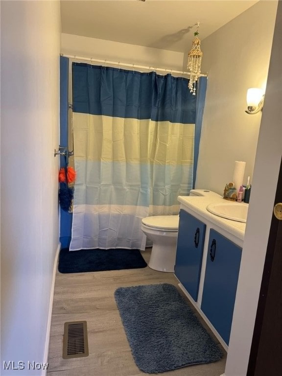 bathroom featuring visible vents, toilet, a shower with shower curtain, wood finished floors, and vanity