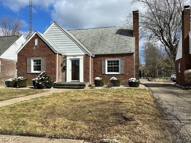 view of front facade with brick siding, a chimney, aphalt driveway, and a front yard