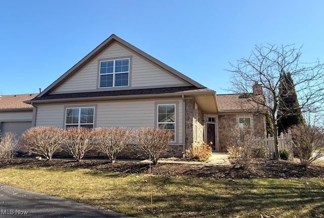 view of front of home featuring a front lawn, stone siding, an attached garage, a shingled roof, and a chimney