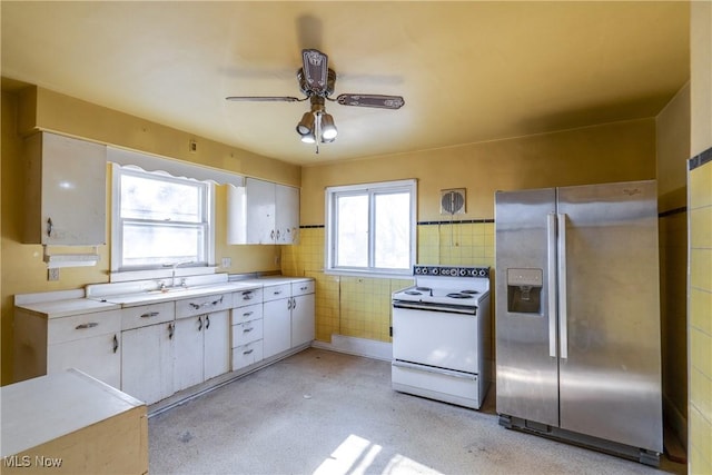 kitchen with a ceiling fan, electric range, light countertops, stainless steel refrigerator with ice dispenser, and tile walls