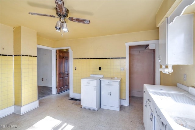 clothes washing area featuring tile walls, a ceiling fan, and wainscoting