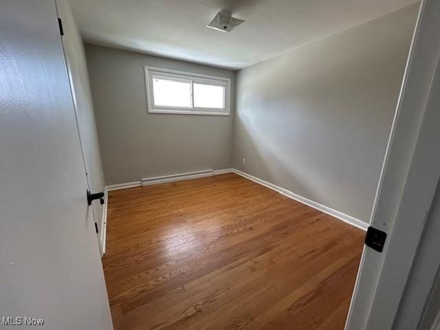 spare room featuring baseboard heating, baseboards, and wood finished floors