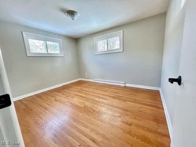 empty room with a baseboard heating unit, baseboards, and wood finished floors