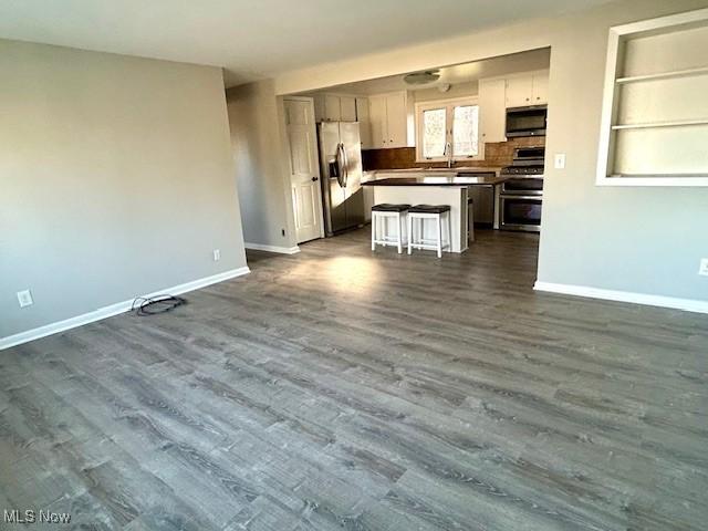 kitchen featuring a kitchen island, open floor plan, appliances with stainless steel finishes, baseboards, and dark wood-style flooring